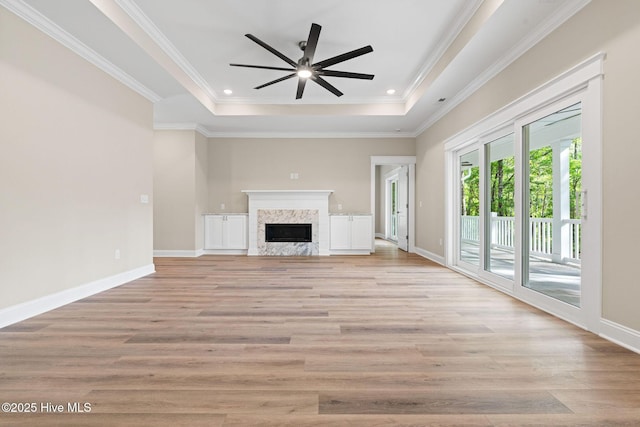 unfurnished living room featuring light wood-style flooring, a premium fireplace, baseboards, a ceiling fan, and a tray ceiling