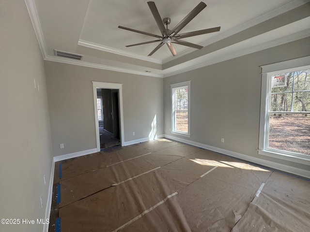 empty room featuring a tray ceiling, visible vents, ornamental molding, a ceiling fan, and baseboards