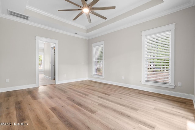 spare room featuring light wood-type flooring, crown molding, a tray ceiling, a ceiling fan, and visible vents