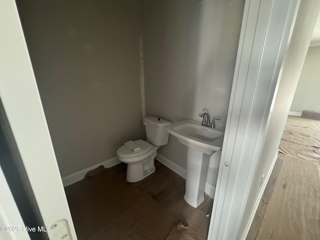 half bathroom featuring toilet, a sink, baseboards, and wood finished floors