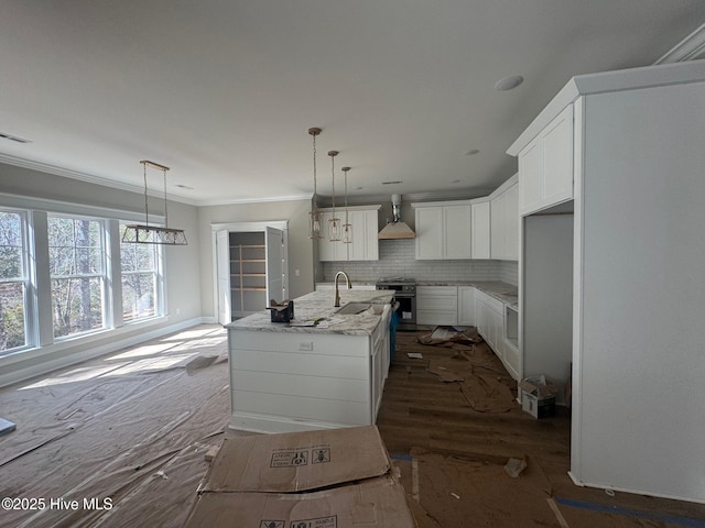 kitchen featuring white cabinets, ornamental molding, backsplash, wall chimney exhaust hood, and an island with sink