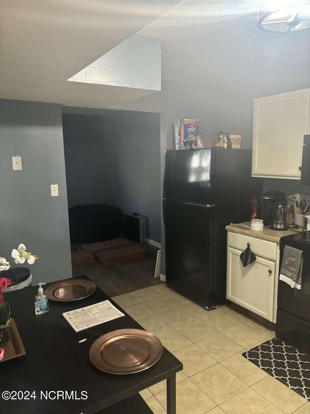 kitchen featuring white cabinetry, black refrigerator, and light tile patterned floors