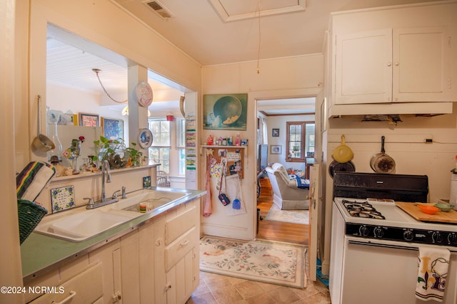 kitchen with white gas stove, sink, light wood-type flooring, white cabinetry, and ornamental molding