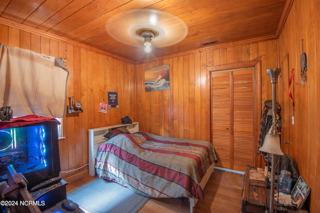 bedroom with a closet, wooden walls, light hardwood / wood-style flooring, wooden ceiling, and ceiling fan