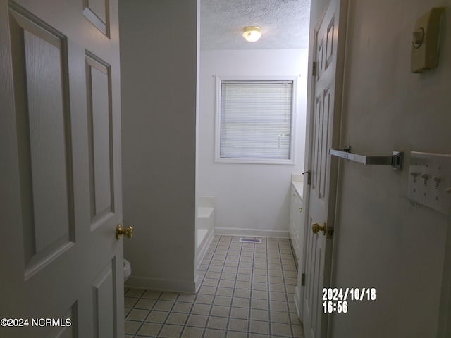 bathroom featuring a tub, toilet, tile patterned flooring, vanity, and a textured ceiling