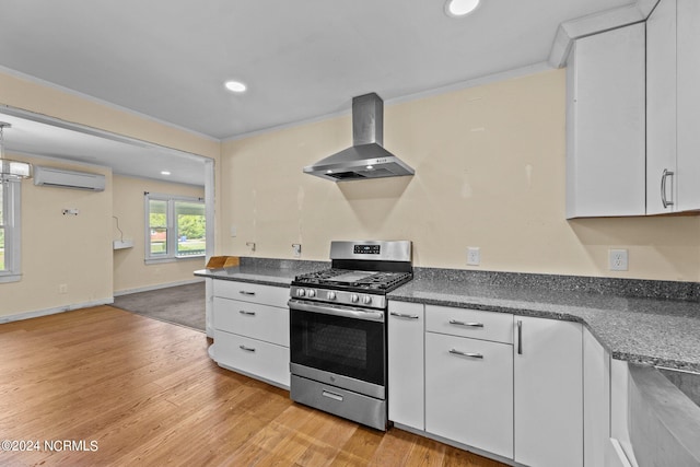 kitchen with white cabinets, gas range, wall chimney range hood, light hardwood / wood-style flooring, and a wall mounted air conditioner