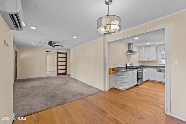 kitchen featuring stainless steel range with gas stovetop, white cabinetry, wall chimney exhaust hood, a barn door, and an AC wall unit