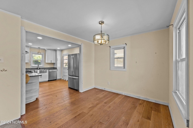 unfurnished dining area with sink, an inviting chandelier, ornamental molding, and light hardwood / wood-style flooring