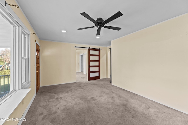 carpeted empty room with a barn door and ceiling fan