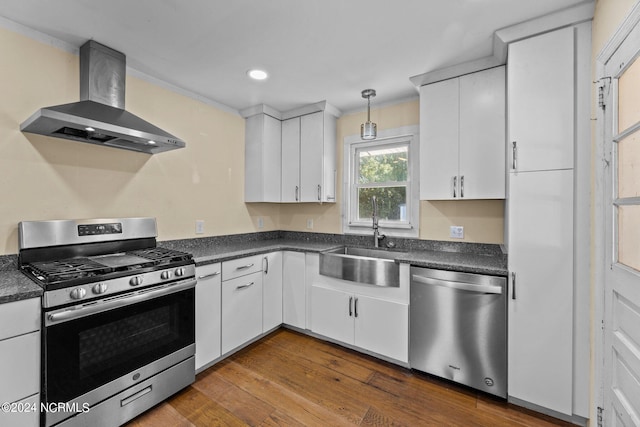 kitchen featuring dark hardwood / wood-style flooring, wall chimney range hood, appliances with stainless steel finishes, and white cabinets