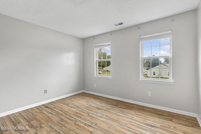 spare room featuring baseboards, a textured ceiling, wood finished floors, and visible vents