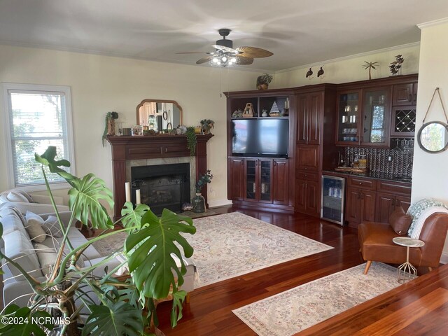 living room featuring wine cooler, ornamental molding, a tiled fireplace, and dark hardwood / wood-style floors