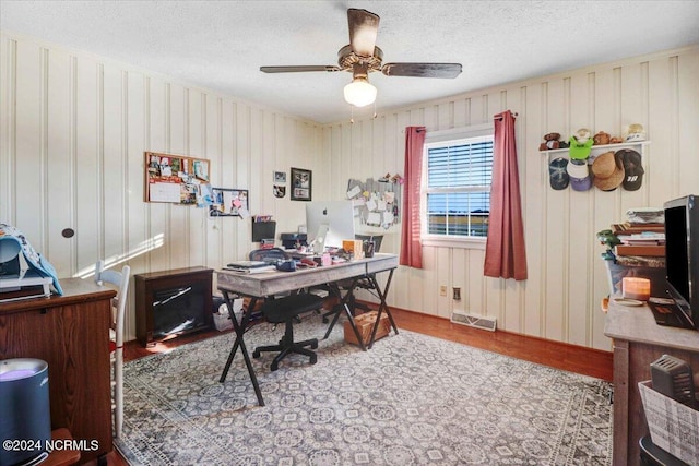 office featuring ceiling fan, a textured ceiling, wooden walls, and light wood-type flooring