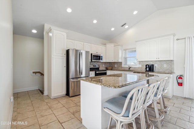 kitchen featuring white cabinetry, a center island, stone countertops, vaulted ceiling, and appliances with stainless steel finishes