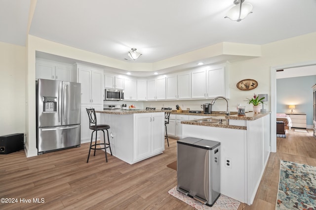 kitchen featuring light hardwood / wood-style flooring, kitchen peninsula, stainless steel appliances, dark stone countertops, and white cabinets