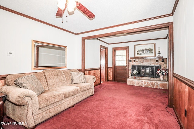 carpeted living room with crown molding, a stone fireplace, wooden walls, and ceiling fan