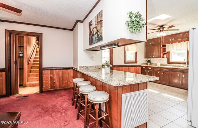 kitchen featuring a textured ceiling, kitchen peninsula, light carpet, ceiling fan, and a breakfast bar