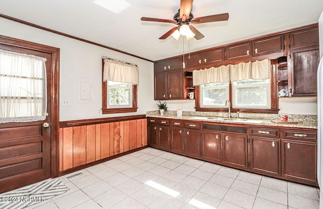 kitchen featuring light tile patterned floors, ceiling fan, ornamental molding, sink, and wooden walls