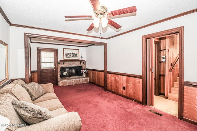 living room featuring carpet, a textured ceiling, a fireplace, crown molding, and wooden walls