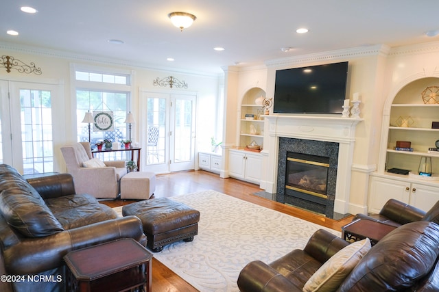 living room with a high end fireplace, crown molding, light hardwood / wood-style flooring, and built in shelves