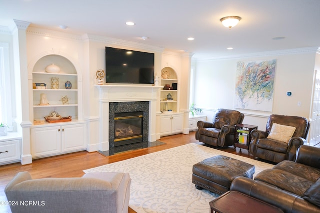 living room featuring light hardwood / wood-style floors, ornamental molding, built in features, and a fireplace