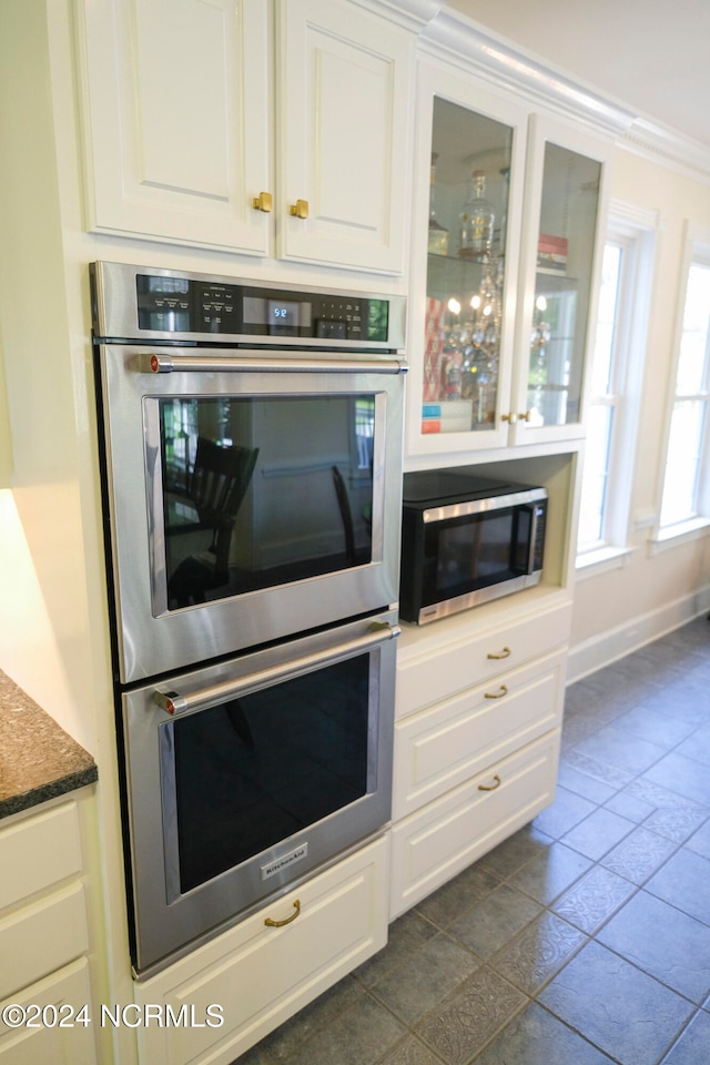 kitchen with white cabinetry, crown molding, stainless steel appliances, and dark tile patterned flooring