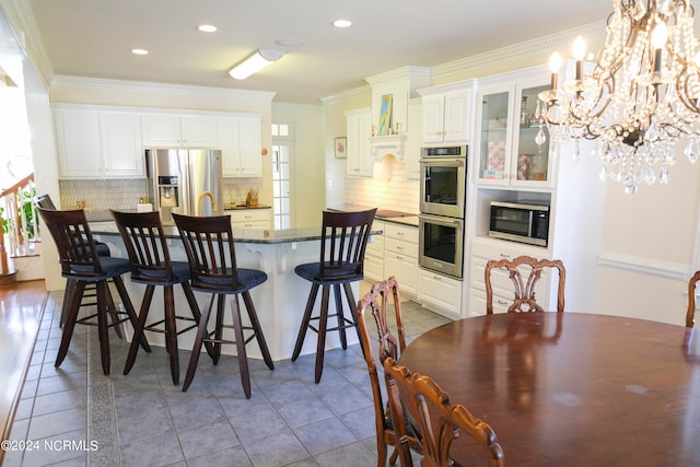 kitchen featuring white cabinets, a notable chandelier, backsplash, appliances with stainless steel finishes, and crown molding