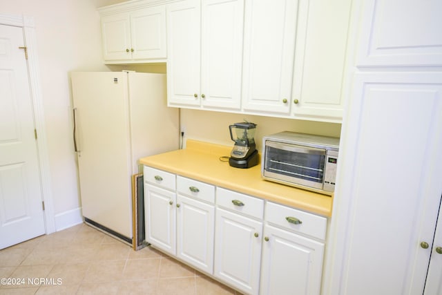 kitchen with light tile patterned flooring, stainless steel microwave, white refrigerator, and white cabinets