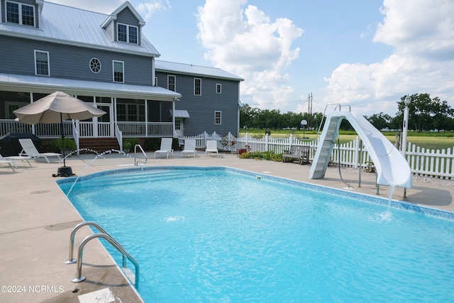 view of swimming pool with a sunroom, a water slide, a water view, and a patio area