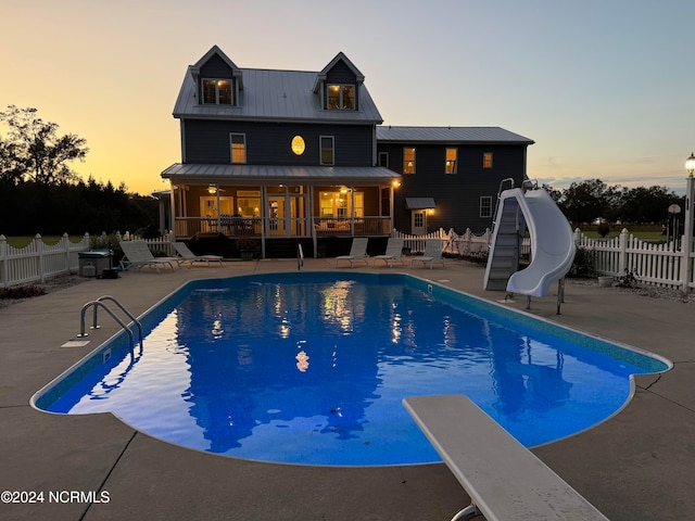 pool at dusk featuring a water slide and a diving board