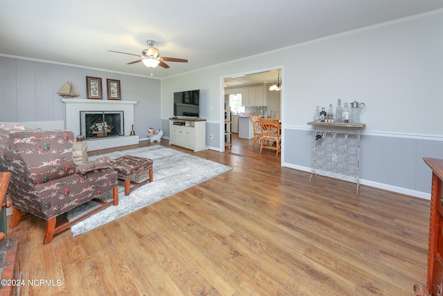 living room featuring crown molding, wood-type flooring, a fireplace, and ceiling fan