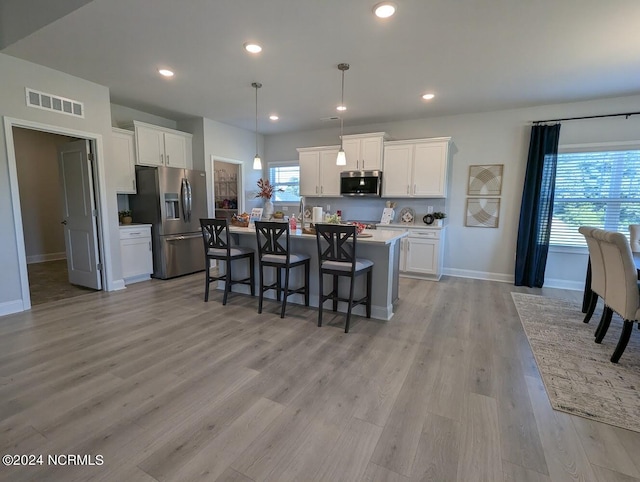 kitchen featuring appliances with stainless steel finishes, white cabinetry, a kitchen island with sink, and pendant lighting