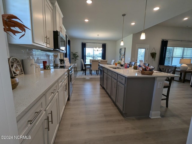 kitchen with sink, white cabinets, decorative light fixtures, appliances with stainless steel finishes, and light hardwood / wood-style floors