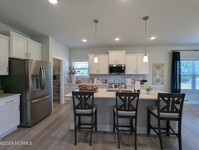 kitchen with a kitchen island with sink, hardwood / wood-style floors, white cabinets, pendant lighting, and appliances with stainless steel finishes