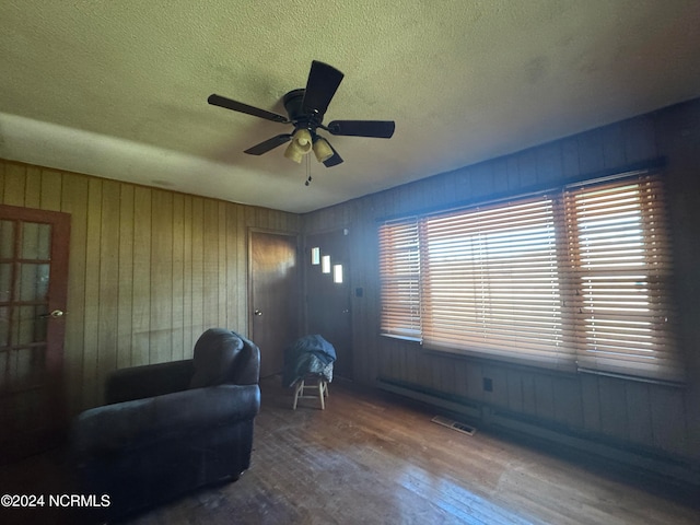 living area with ceiling fan, wooden walls, a textured ceiling, and hardwood / wood-style flooring