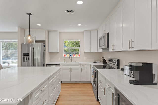 kitchen with hanging light fixtures, white cabinetry, sink, light hardwood / wood-style floors, and stainless steel appliances