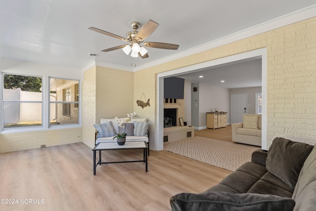 living room featuring ceiling fan, ornamental molding, light hardwood / wood-style flooring, and a fireplace