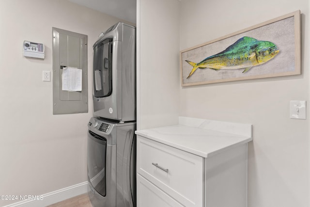 laundry area with electric panel, stacked washer and dryer, light hardwood / wood-style flooring, and cabinets