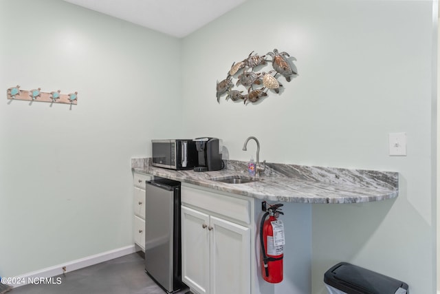 kitchen with stainless steel fridge, white cabinets, sink, and light stone countertops