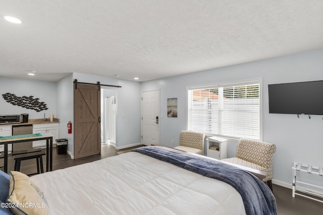 bedroom featuring a textured ceiling, a barn door, and dark hardwood / wood-style flooring