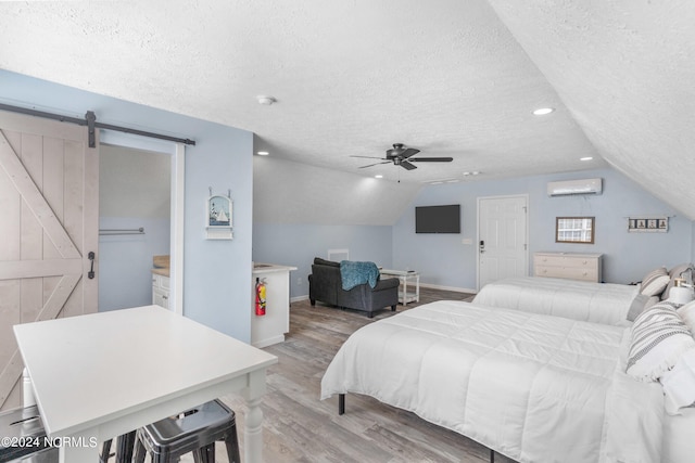 bedroom with a wall mounted AC, light hardwood / wood-style flooring, vaulted ceiling, a barn door, and ceiling fan