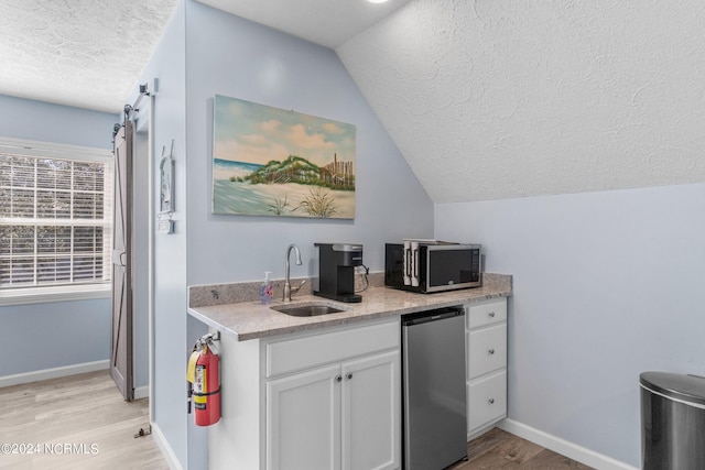 kitchen featuring sink, light wood-type flooring, stainless steel appliances, lofted ceiling, and white cabinets