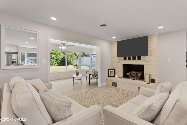 living room with a fireplace, light wood-type flooring, and ceiling fan