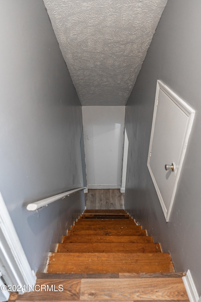 stairs with hardwood / wood-style floors, a textured ceiling, and vaulted ceiling