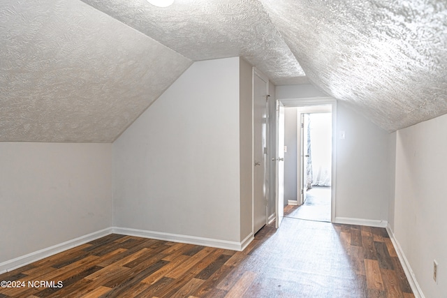 additional living space featuring dark hardwood / wood-style floors, a textured ceiling, and vaulted ceiling