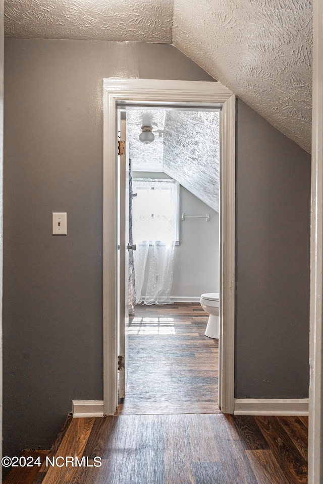 hallway with lofted ceiling, a textured ceiling, and dark hardwood / wood-style floors