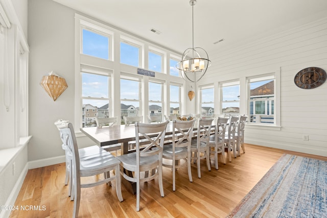 dining area with wooden walls, an inviting chandelier, light hardwood / wood-style flooring, and a healthy amount of sunlight