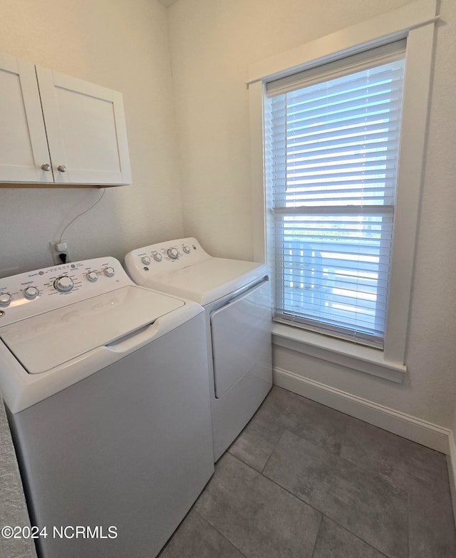 clothes washing area with cabinets, dark tile patterned flooring, and washing machine and clothes dryer