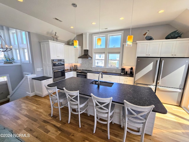 kitchen with lofted ceiling, a center island with sink, sink, wall chimney exhaust hood, and stainless steel appliances