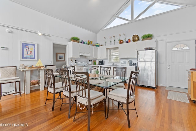 dining room with a skylight, high vaulted ceiling, and light hardwood / wood-style floors